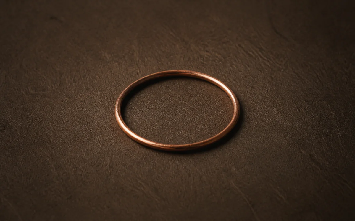Thin copper ring casting a soft glow across textured espresso paper